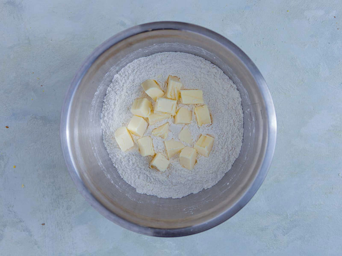 Cubes of cold butter sitting on top of flour in a stainless steel mixing bowl before being cut in.
