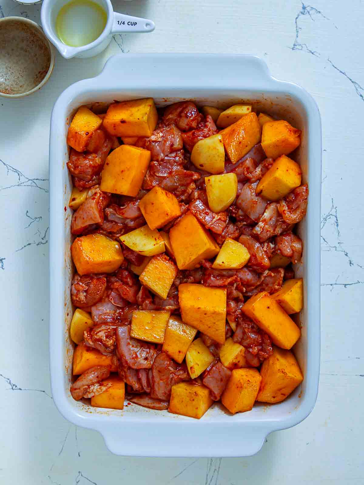 Marinated chicken, pumpkin, and potato mixture spread in a white 9x13 baking dish before going into the oven.