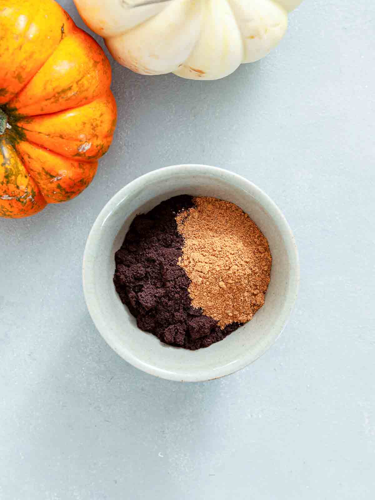 A small bowl holding dark coffee grounds on one side and a mound of pumpkin pie spice on the other.