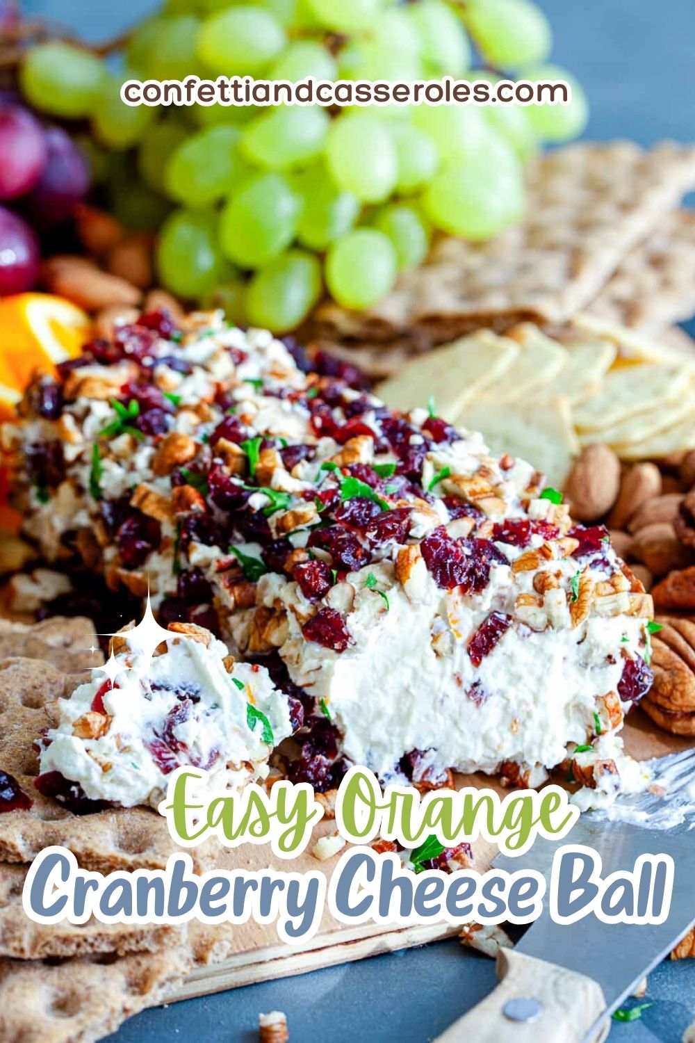 Pinterest pin of an orange cranberry cheese ball with a pecan and cranberry crust, cut open on a board with grapes and crackers, under the title Easy Orange Cranberry Cheese Ball.