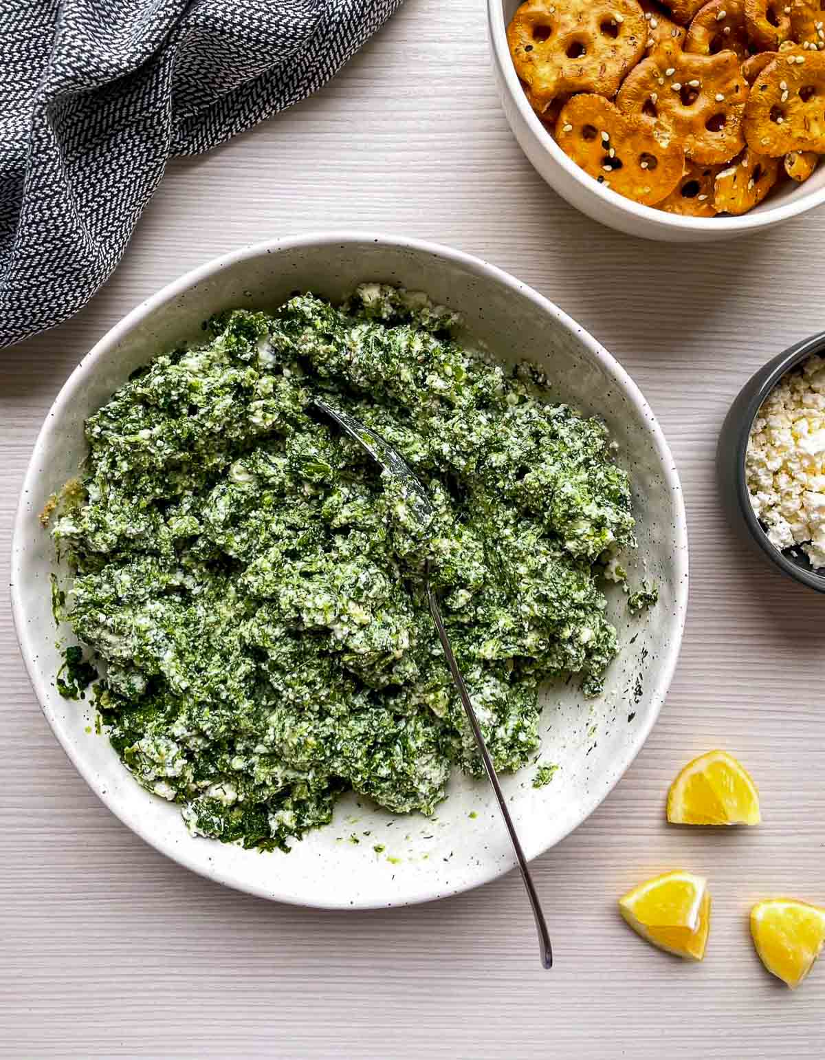 A creamy green spinach and ricotta mixture stirred together in a white bowl with a spoon resting in it.